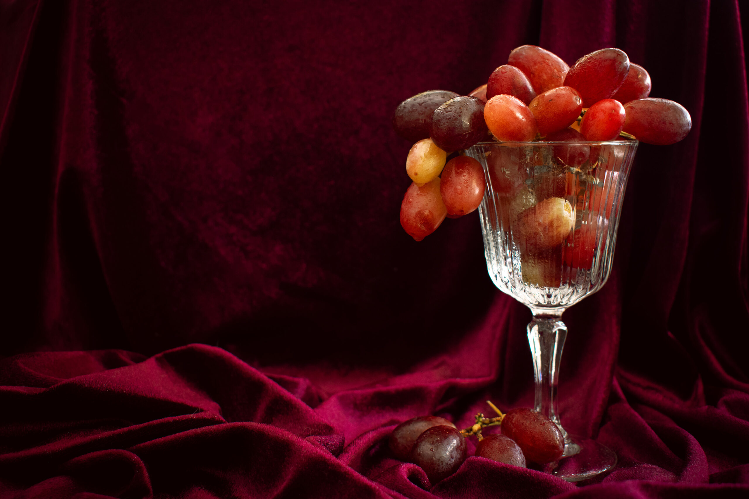 A photography example of grapes in a wine glass with velvet background, taken by Ginj Studio
